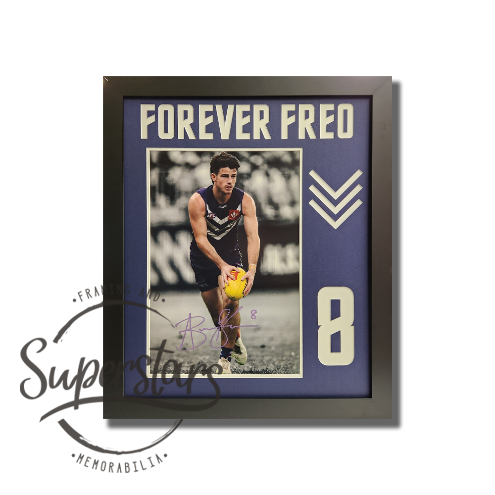 Andrew Brayshaw memorabilia: A photo of Andrew about to kick a football during a game. The background is black and white and Andrew is full colour. It has been framed with a purple border and black timber frame. Across the top Forever Freo has been cut into the matting, in white. Down the side is Andrew's number 8. Andrew has signed the photo in purple ink.