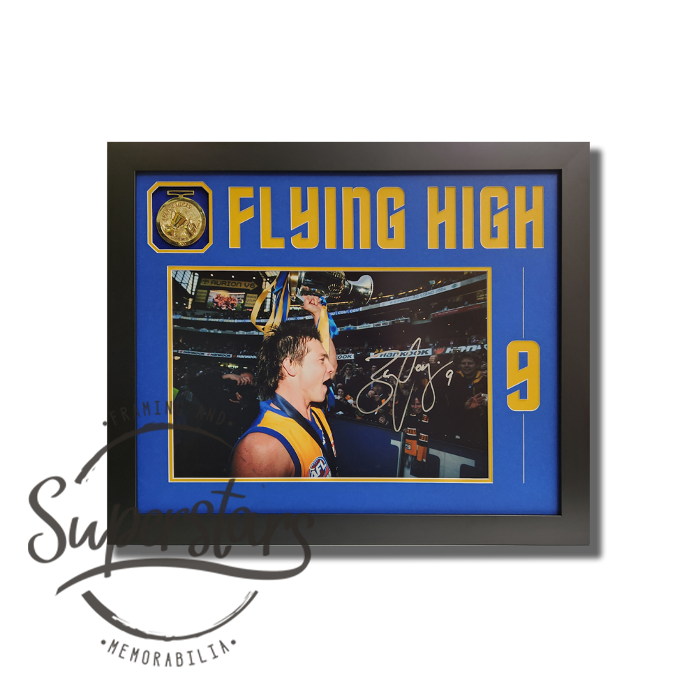 Ben Cousins memorabilia Perth. A photo of Ben Cousins waving to the crowd and wearing his premiership medal. It has been framed with a blue border and black timber frame. In the left corner is a replica medal. Across the top Flying High has been cut into the matting, in yellow. Down the side is Ben's number 9. Ben has signed the photo in silver ink.