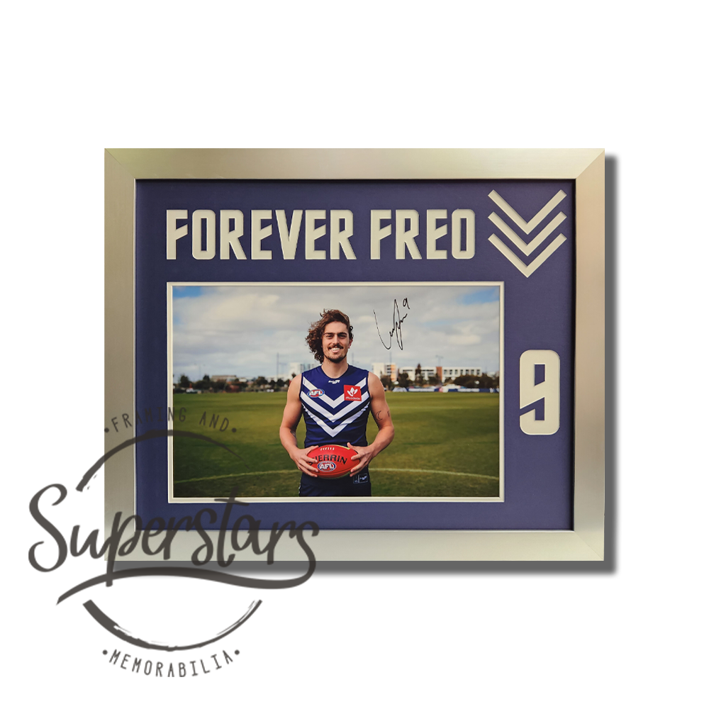 Luke Jackson memorabilia: A photo of Luke holding a football on the field. It has been framed with a purple border and silver timber frame. Across the top Forever Freo has been cut into the matting, in white. Down the side is Luke's number 9. Luke has signed the photo in black ink.