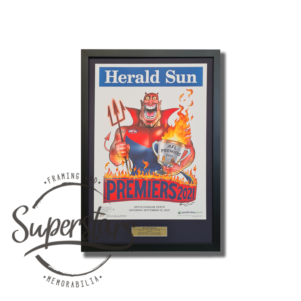 Melbourne Premiership Memorabilia. 2021 AFL Premiers. A cartoon demon is the main feature, with the word Premiers across the bottom. This has been framed with a black border, black timber frame and plaque.